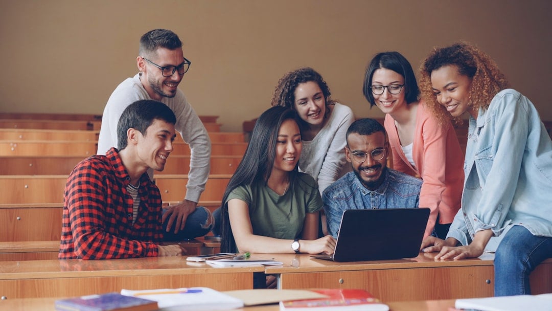 Diverse group of adult students collaborating around a laptop in an English language school classroom in Canada