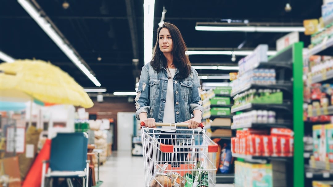 Young woman pushing a shopping cart through a grocery store aisle budgeting monthly expenses in Canada