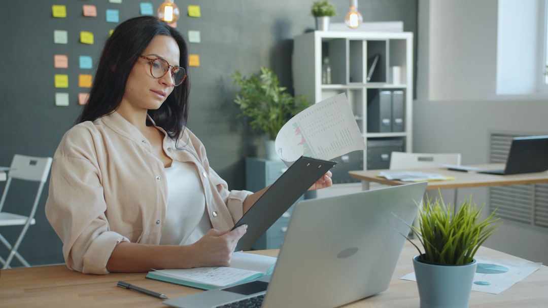 Young woman reviewing study permit documents at a desk with laptop and clipboard