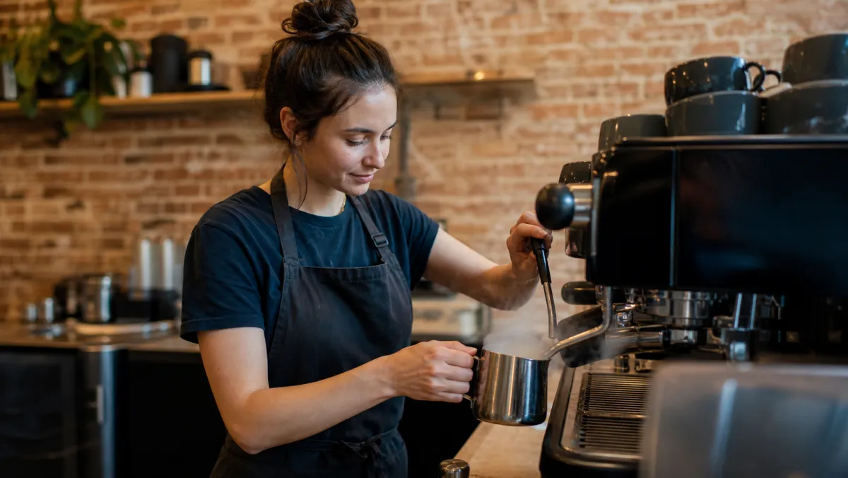 International student working a part-time cafe job in Canada, steaming milk at an espresso machine
