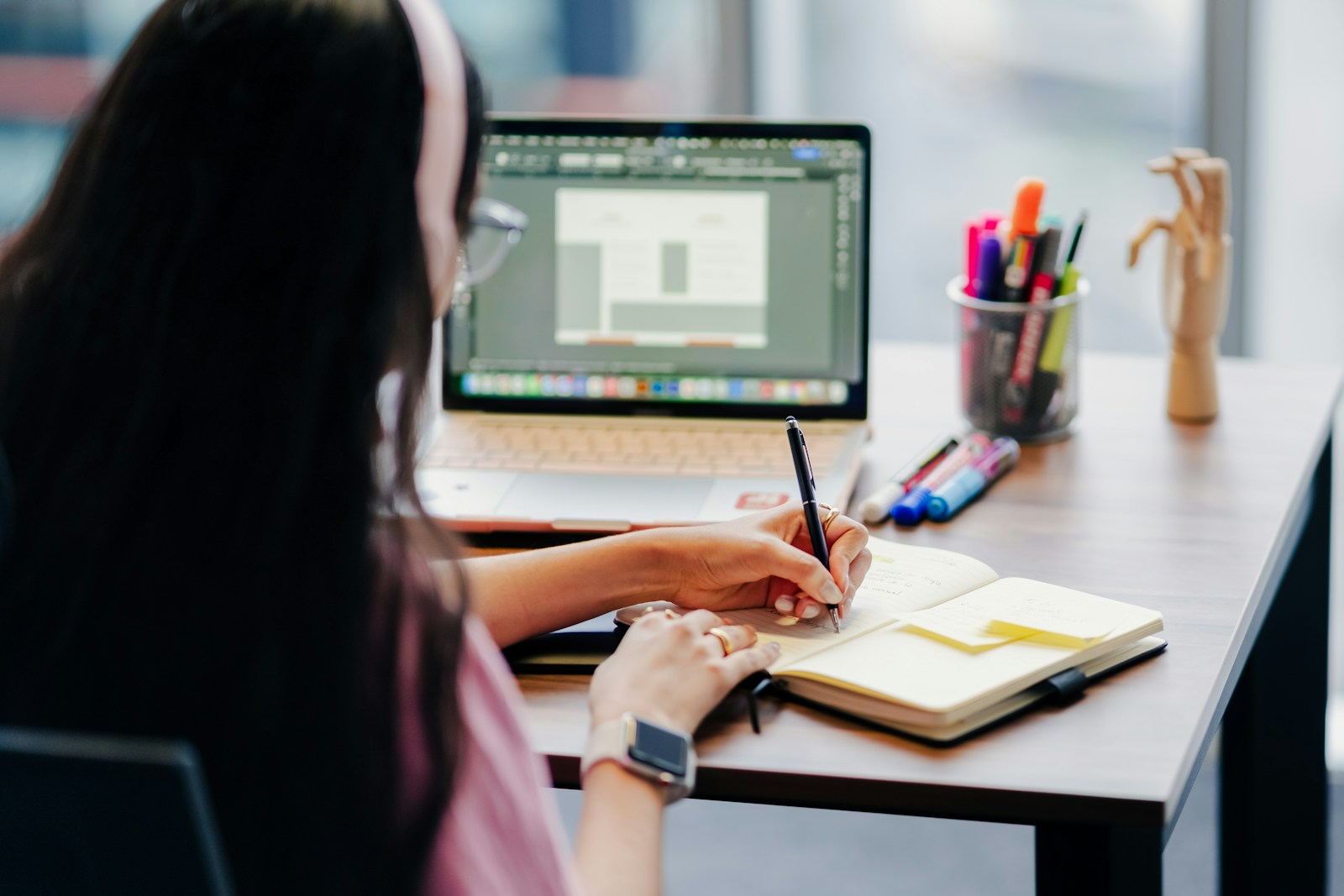 Young adult comparing French program options on a laptop while taking handwritten notes in a journal