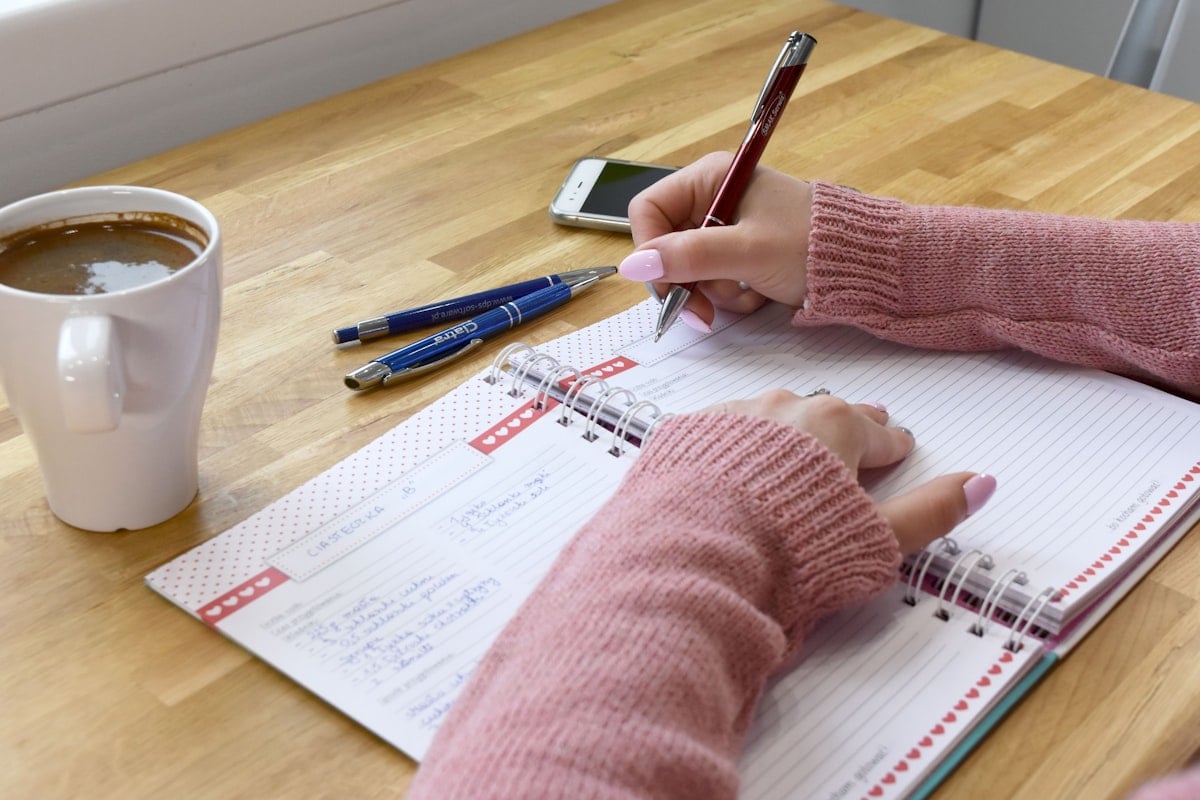 Hand writing in an open planner notebook beside a coffee mug and phone, working through a PGWP action checklist